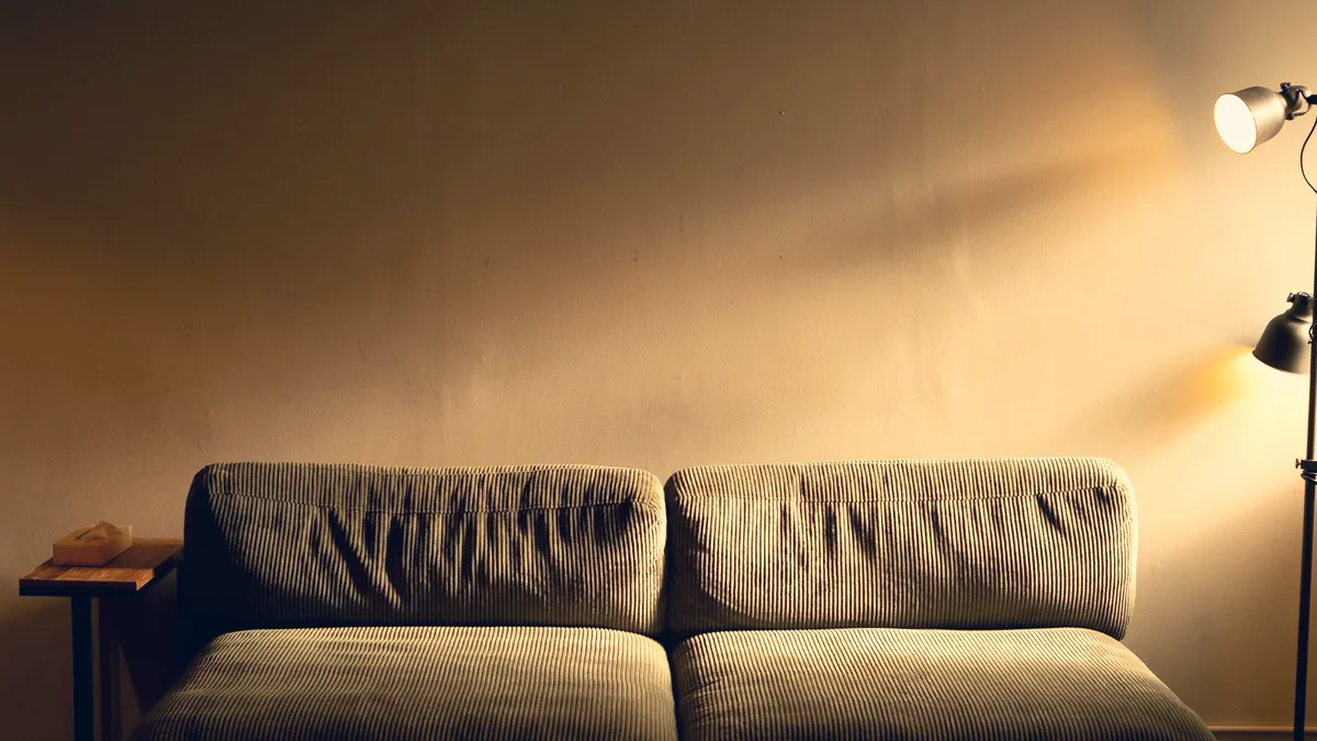 Un canapé vide dans un salon, le soir, sous la lumière d'une lampe restée allumée.