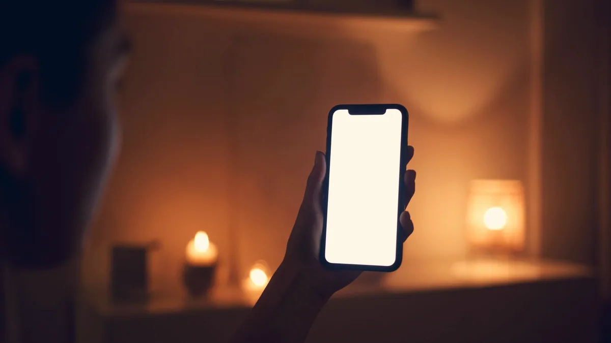 Une main tenant un téléphone dans une pièce sombre.