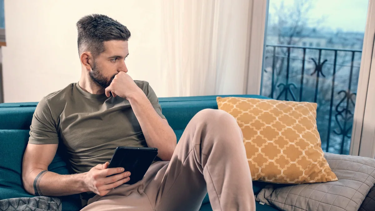 Une personne assise dans un canapé, une tablette à la main.