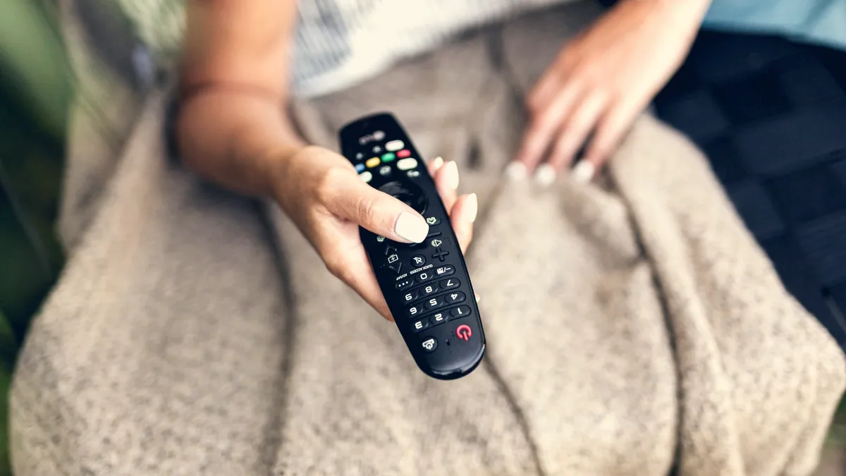 Une personne assise dans un canapé, télécommande à la main.